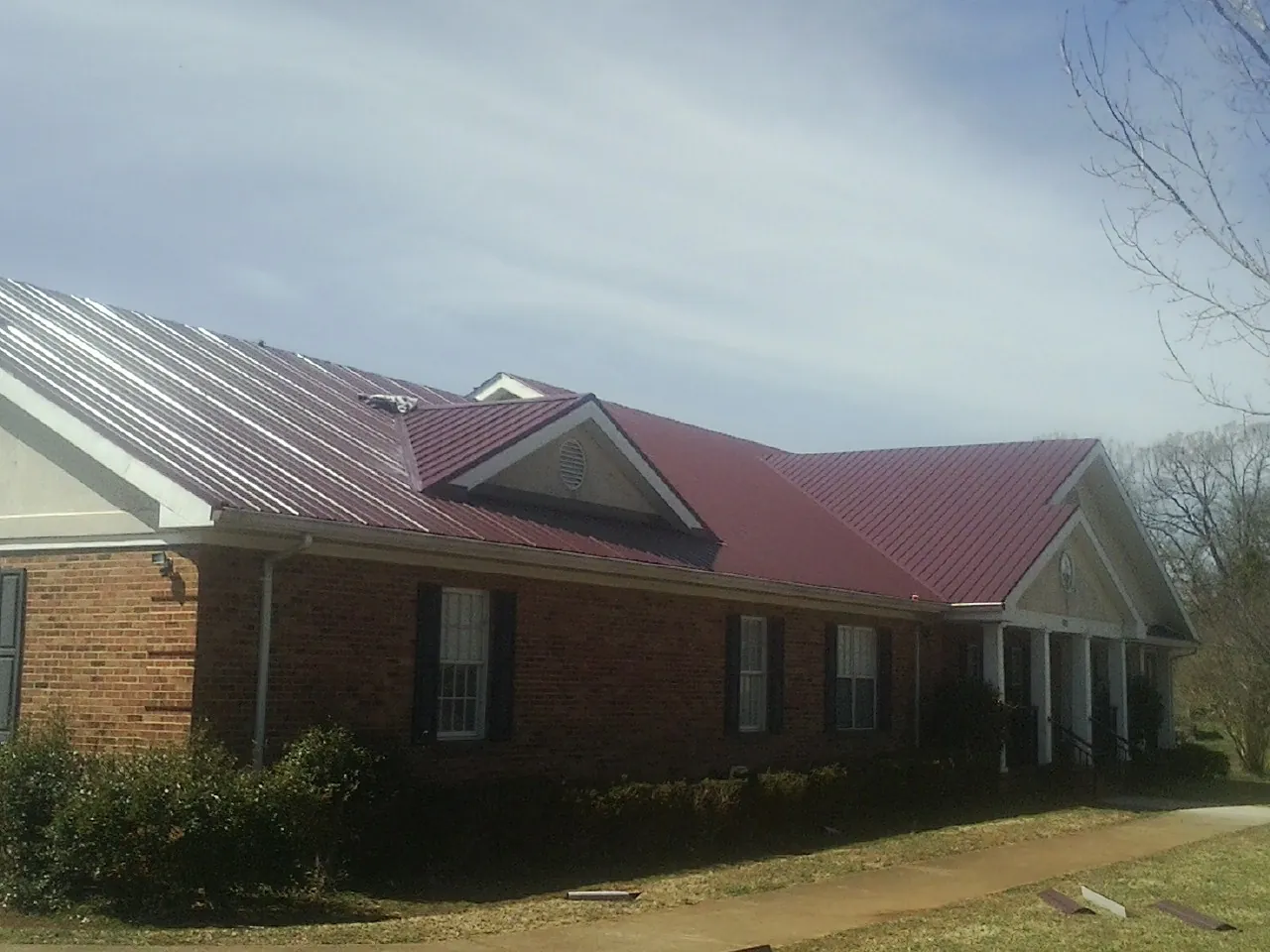 Red metal roof with gabled entries on a long brick building, from a Hail Damage Roof Repair job in Brandywine