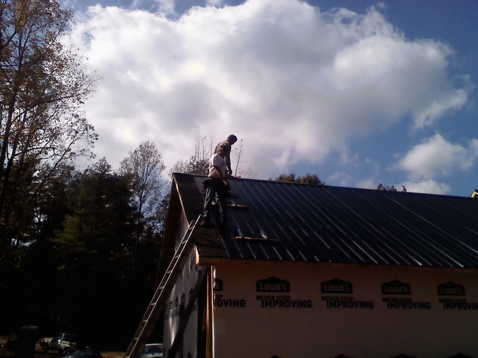Roofer fastening dark metal panels high against a cloudy sky, from a Roof Inspection job in Brandywine